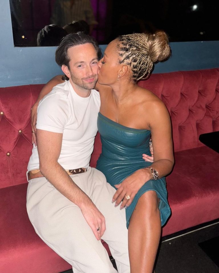 Mel B kissing Rory McPhee on the cheek while sitting on a red couch.