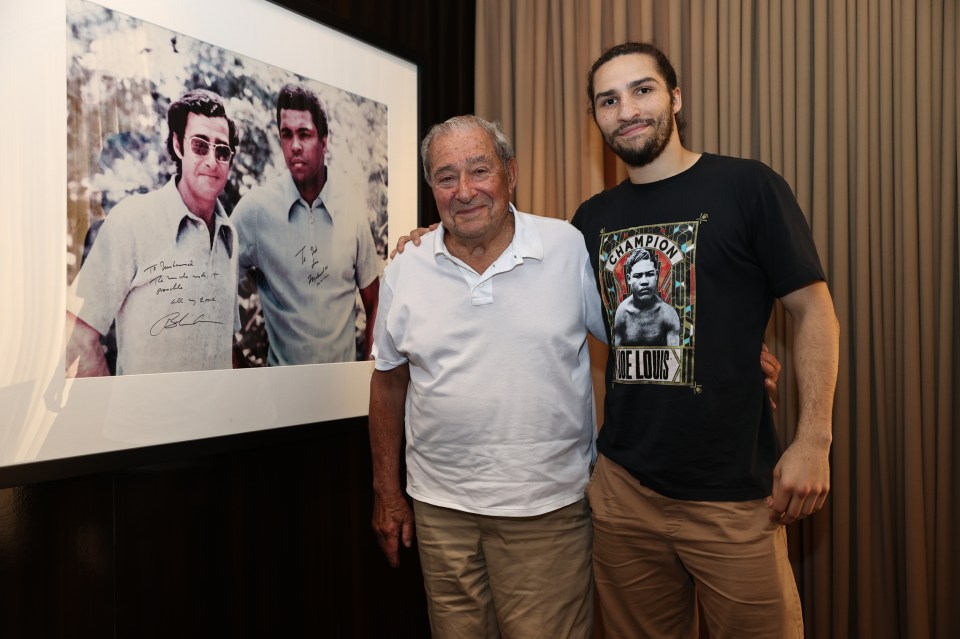 Two men posing with a signed photo of Muhammad Ali and another man.