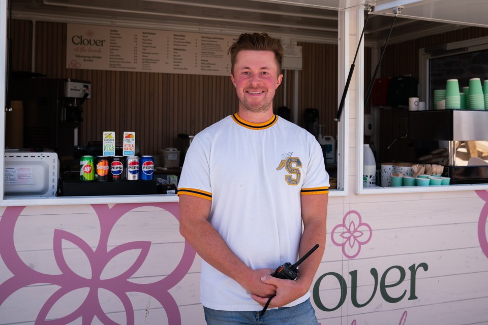 Man holding a walkie-talkie in front of a beachside kiosk.