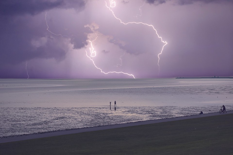 Lightning storm over the sea with people watching.