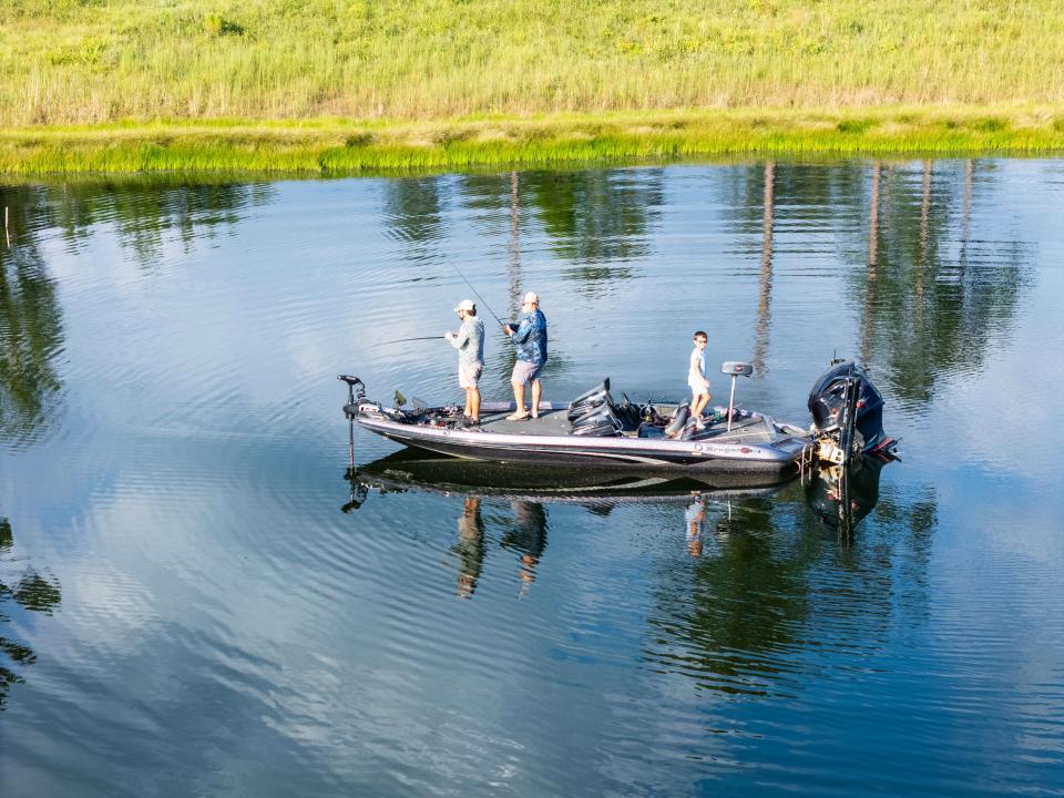 Three people fishing from a bass boat on a calm lake.
