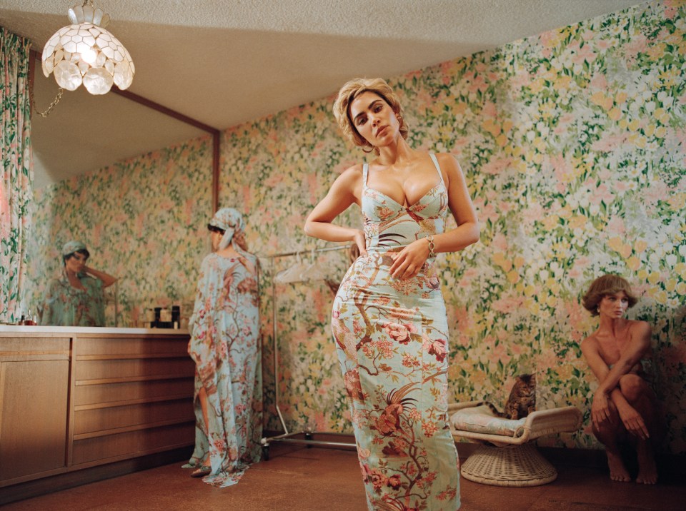 Woman in floral dress in a vintage room with two other women and a cat.
