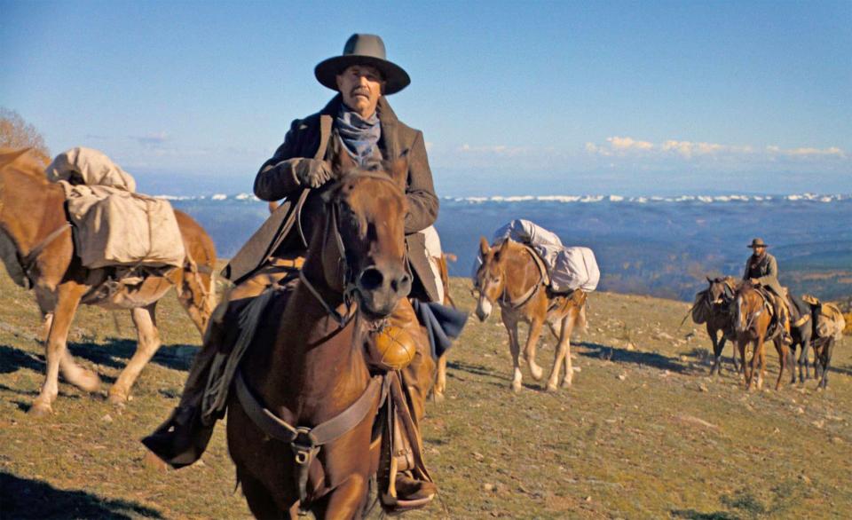 Kevin Costner on horseback leading a pack train across a mountain landscape.