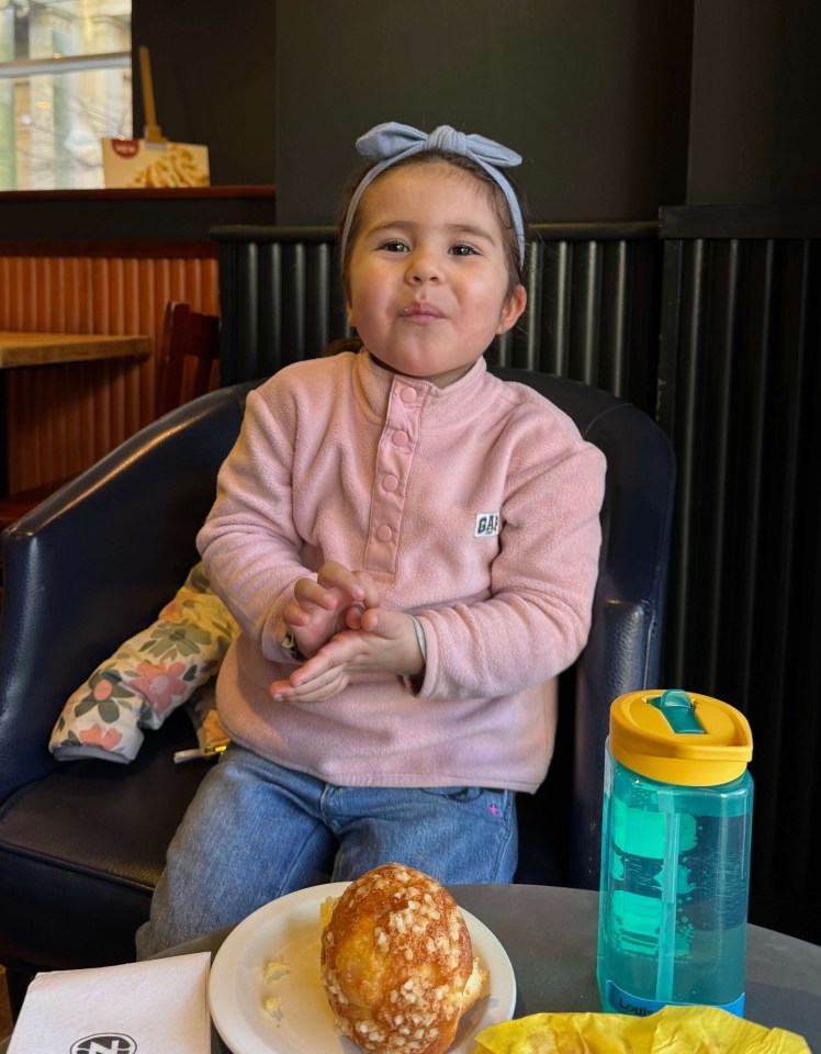 A young girl sits in a chair, eating a pastry.