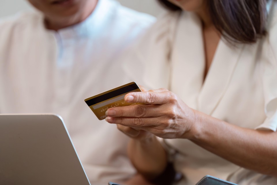 Close-up of a person's hands holding a credit card and using a laptop.