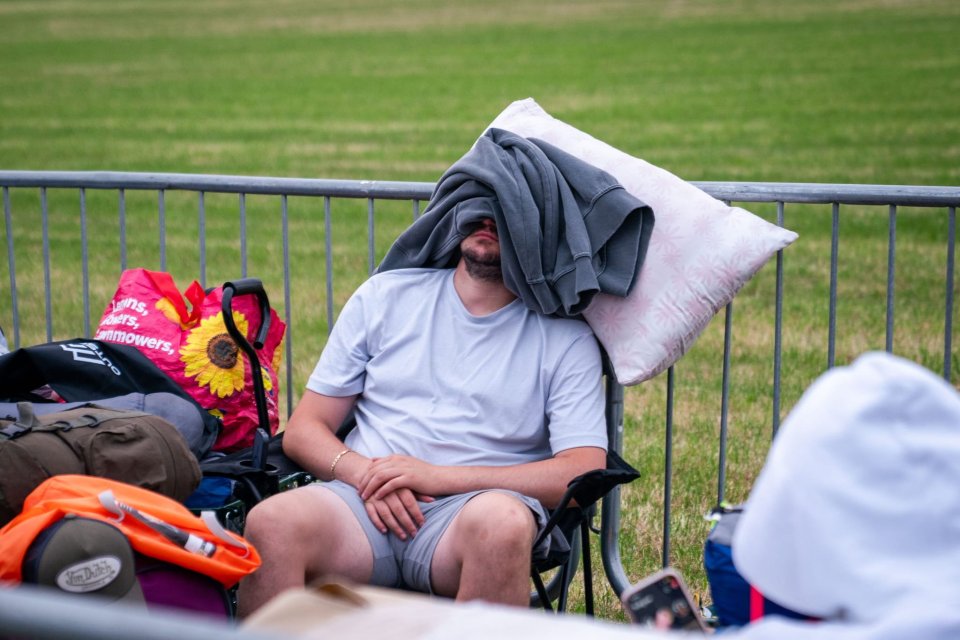 Person sleeping at a festival with belongings nearby.