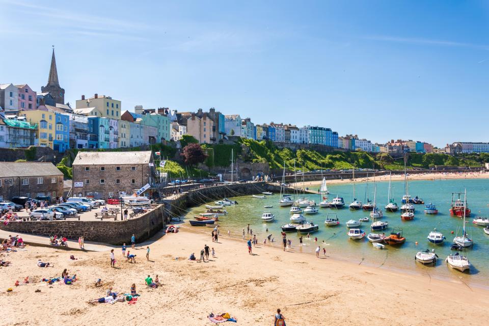 Tenby harbor with boats and people on the beach.