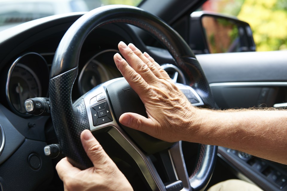A man's hand hitting a car horn.