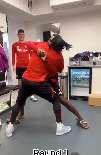 Two soccer players playfully wrestling in a locker room.  "Round 1" is visible at the bottom.