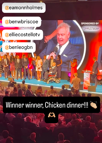 Screenshot of an awards ceremony with winners on stage and audience; social media handles are tagged.