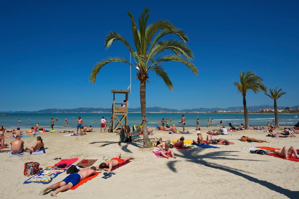 Beach scene in Playa de S'Arenal, Majorca, with people sunbathing and swimming.