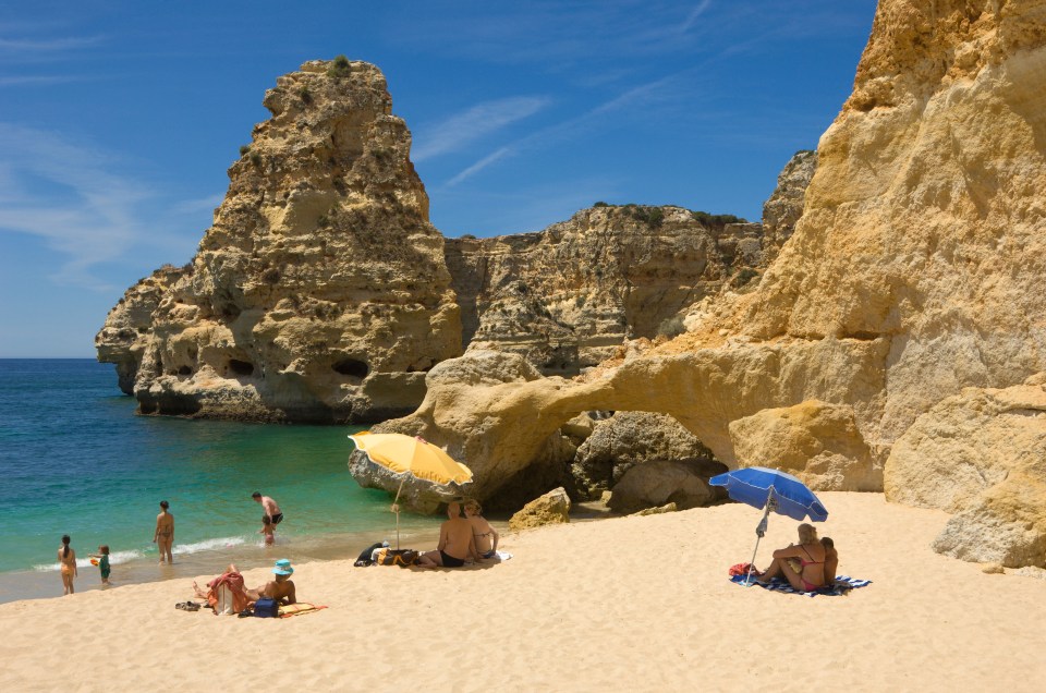 Beach scene in Algarve, Portugal, with people relaxing under umbrellas.