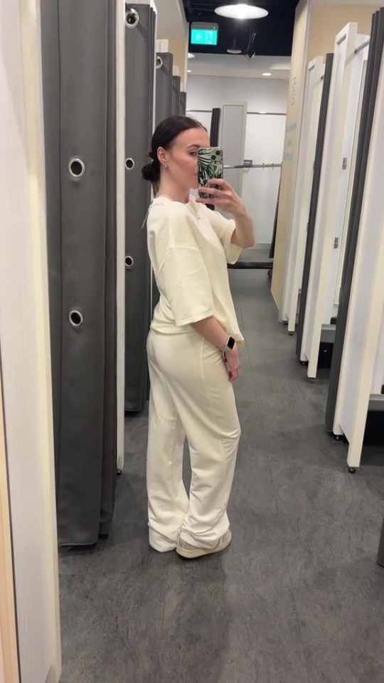 Woman in a cream-colored tracksuit in a Primark changing room.