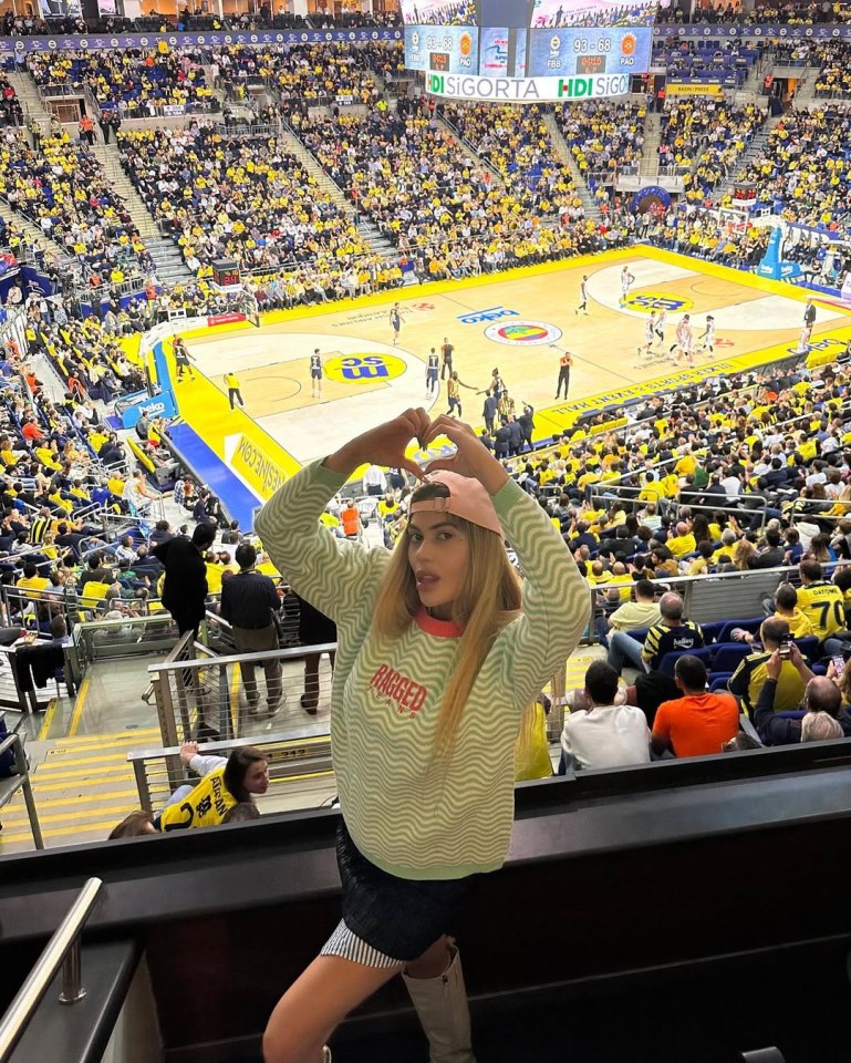 Woman making heart shape with hands at a basketball game.