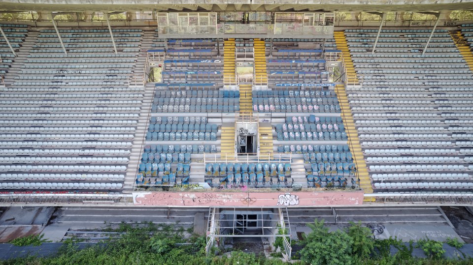 Aerial view of the abandoned Flaminio Stadium in Rome, Italy, showing overgrown vegetation and graffiti.