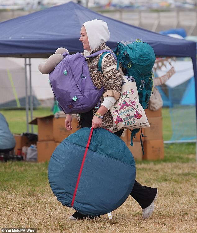 Revellers arrive at the Glastonbury Festival during a rain shower at Worthy Farm this morning