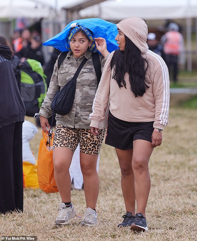 Revellers arrive at the Glastonbury Festival during a rain shower at Worthy Farm this morning