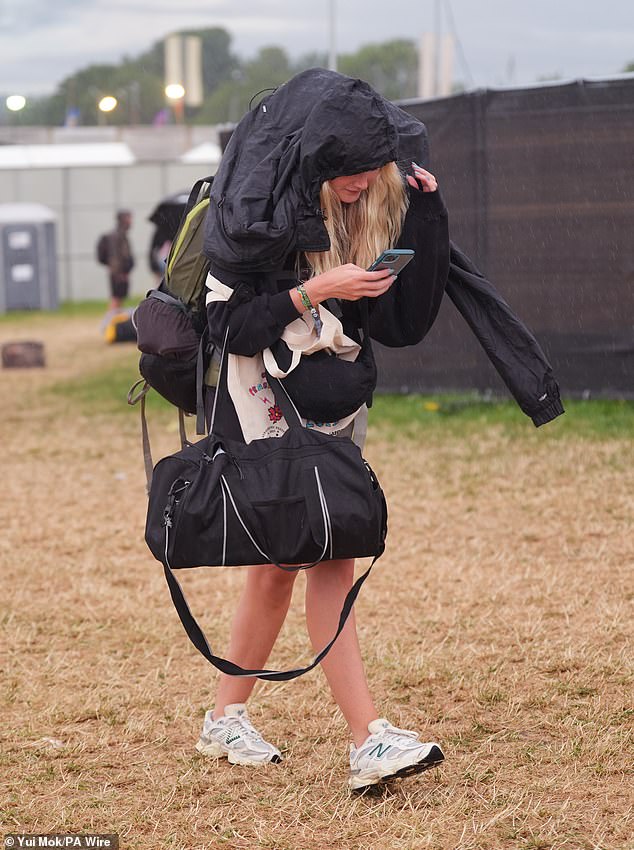 Revellers arrive at the Glastonbury Festival during a rain shower at Worthy Farm this morning