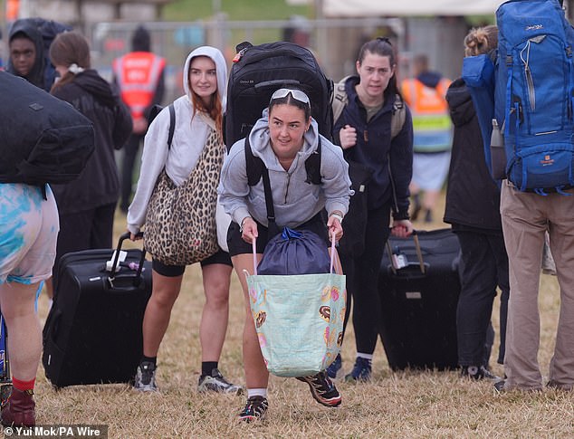 Revellers arrive at the Glastonbury Festival during a rain shower at Worthy Farm this morning