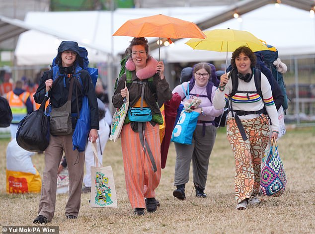 Revellers arrive at the Glastonbury Festival during a rain shower at Worthy Farm this morning