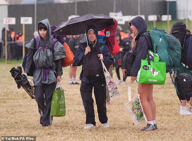 Revellers arrive at the Glastonbury Festival during a rain shower at Worthy Farm this morning