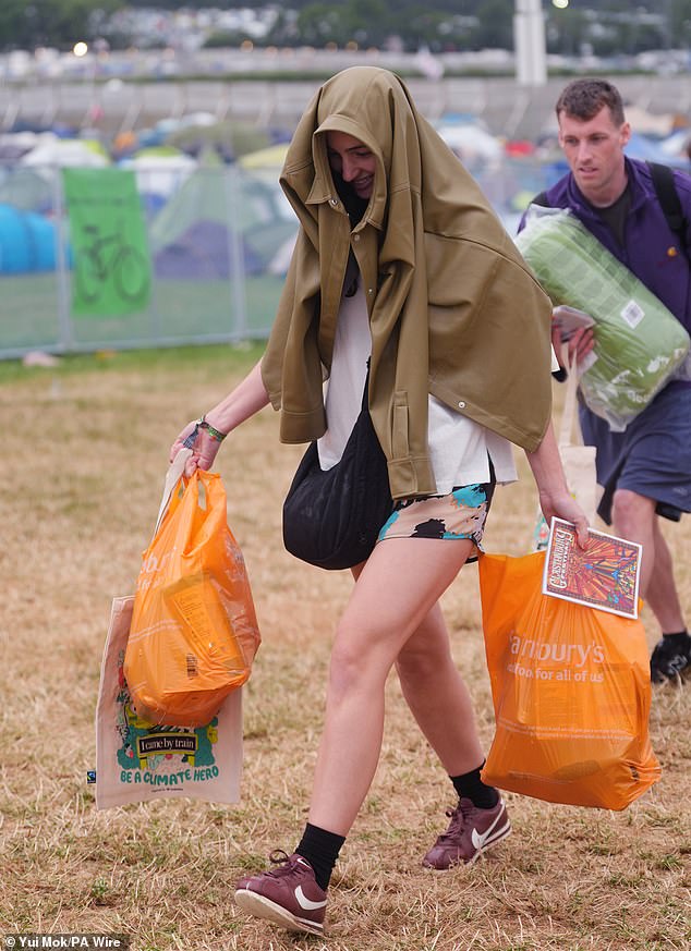 Revellers arrive at the Glastonbury Festival during a rain shower at Worthy Farm this morning