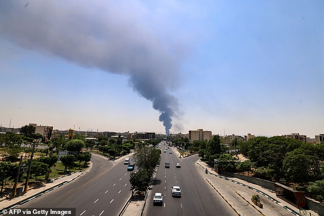Commuters drive along a road as a plume of heavy smoke and fire rise from an oil refinery in southern Tehran, after it was hit in an overnight Israeli strike, on June 15, 2025
