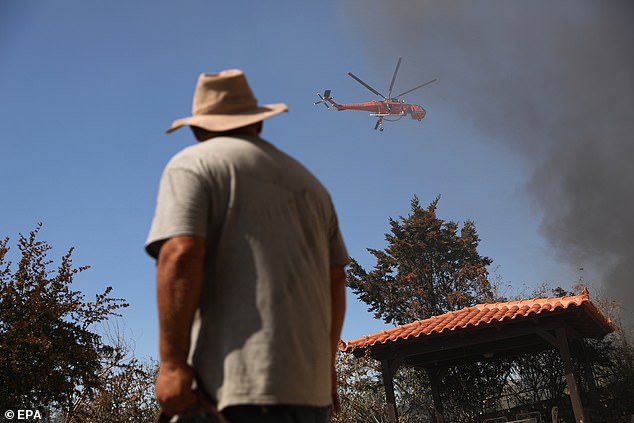 A resident watches a firefighting helicopter as it battles a wildfire burning in the coastal region of Palaia Fokaia, some 40km southeast of Athens, Greece, 26 June 2025