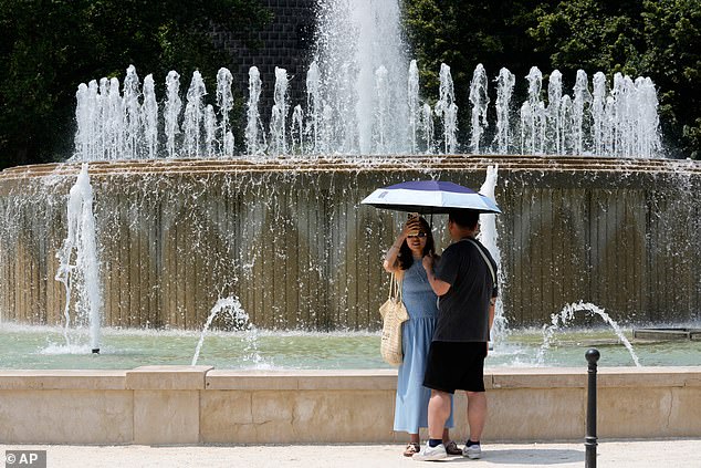 ITALY: Temperatures are also soaring over 40 degrees in Italy, the Balkans and Turkey. Pictured: Tourists shelter from the hot sun next to a fountain at the Sforzesco Castle in Milan