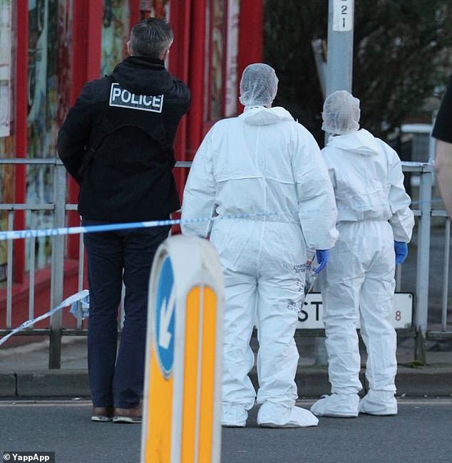 Police officers in white forensics gear stand within a cordon at the scene of the stabbing in Bradford