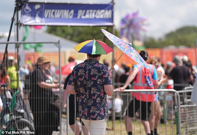 A festivalgoer holds a parasol to shield from the sun alongside a daring umbrella hat