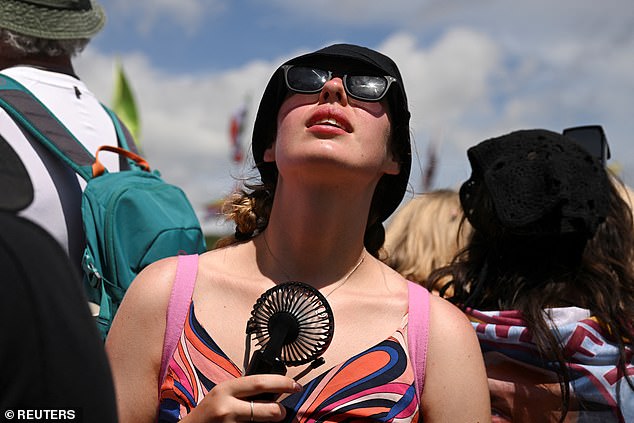 A woman uses a portable fan to try and beat the hot weather at Glastonbury Festival