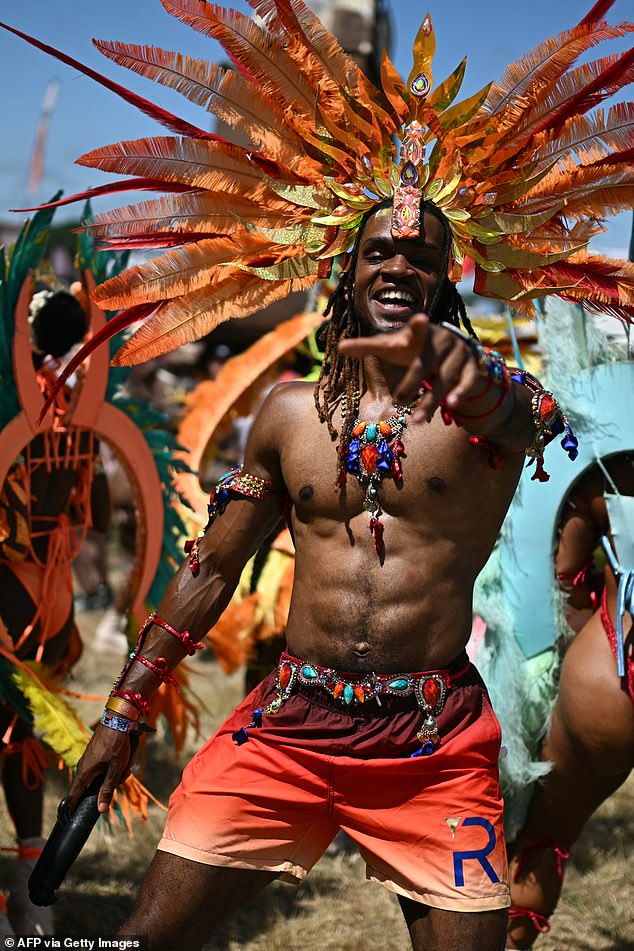 A joyful Notting Hill dancer wearing feathers in his hair beams at the camera as they perform