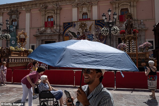 SPAIN: A man carries a parasol as he walks in the Plaza de la Virgen where Corpus Christi sculptures are on display as parts of Spain experience a heatwave on June 21, 2025 in Valencia, Spain