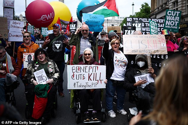 Protesters sitting in wheelchairs hold placards reading messages like "Benefit cuts kill" as they take part in a "No More Austerity 2.0" march in central London on June 7