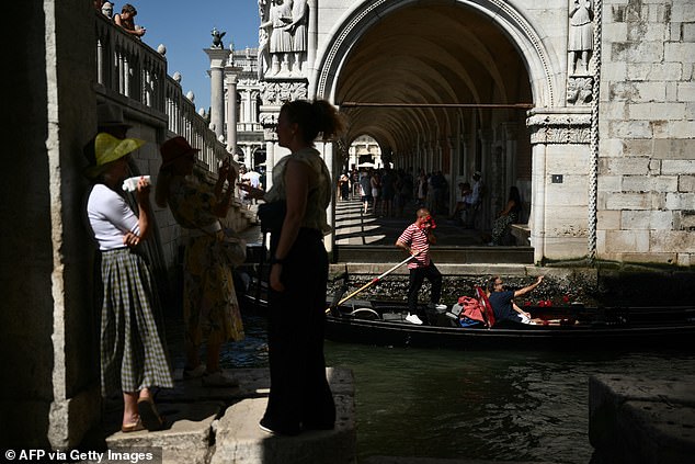 Tourists look for shade on a hot summer day in Venice as Europeans have been warned to stay indoors as the continent goes on high alert for extreme 47C heat