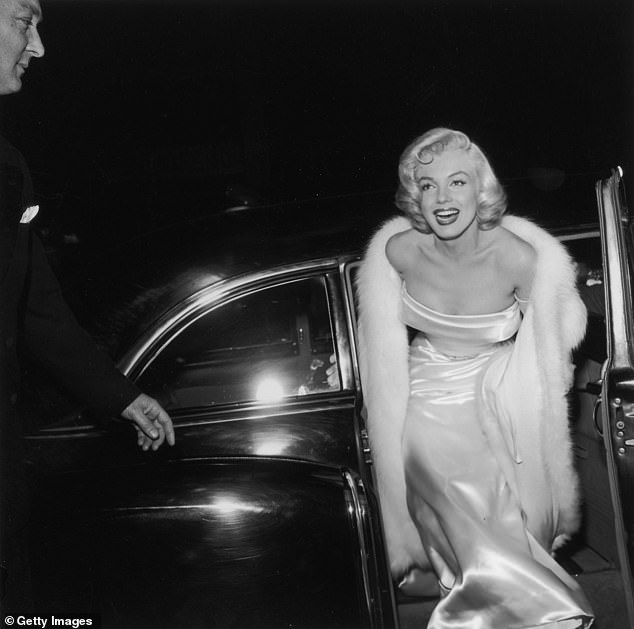 Marilyn Monroe emerges from a car in a strapless white gown and white fur coat at the premier of 'There's No Business Like Show Business'