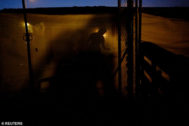 Pictured: The silhouette of a woman is pictured as she cooks inside her shack of a makeshift settlement Can Rova 2