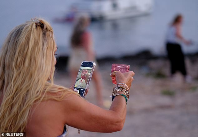 The island's council has recently introduced a major new rule designed to combat overtourism. Pictured: A tourist takes a picture of her glass on the north central coast of Ibiza, Spain