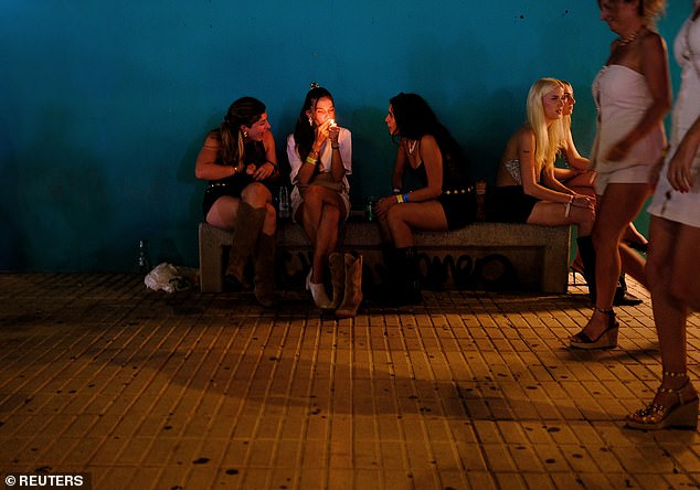Tourists sit on a bench before walking towards a discotheque near Playa d'en Bossa beach
