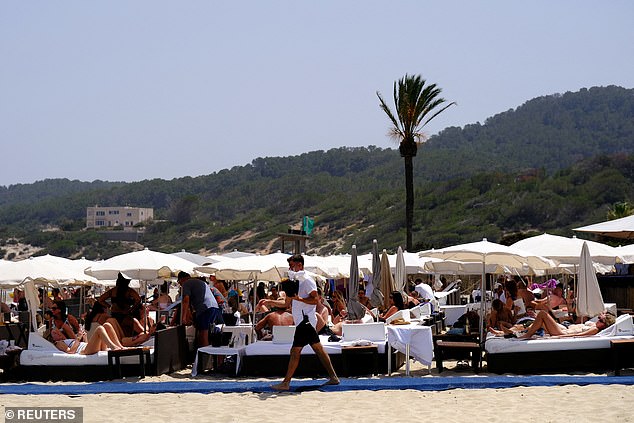 A waiter carries drink to the tourists as they sunbathe at Playa d'en Bossa beach