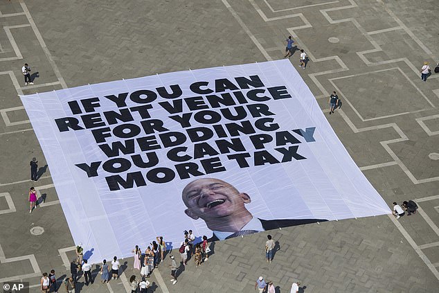 This photo released by Greenpeace shows a large banner against Amazon founder Jeff Bezos' planned wedding, in St. Mark Square, in Venice, Italy Monday, June 23