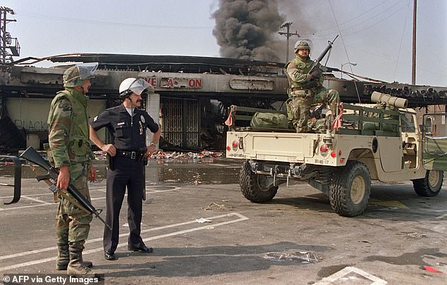 National Guardsmen and a police officer take up security positions in front of a burned and looted shopping center