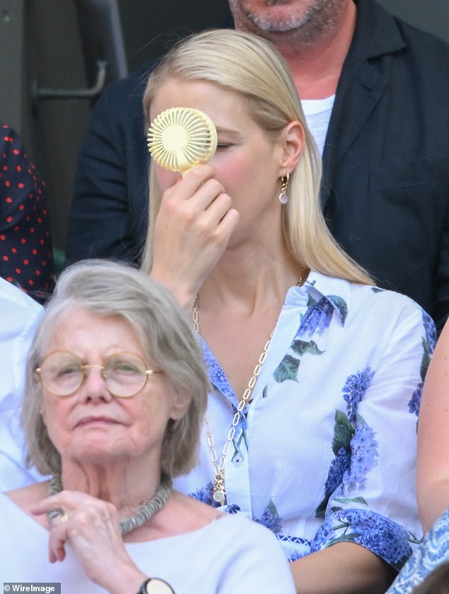 She put her best fashion foot forward in a white collared frock printed with delicate lilac flowers as she discussed the match with Robert while also waving a portable fan in front of her face to keep her cool in the 33-degree heat