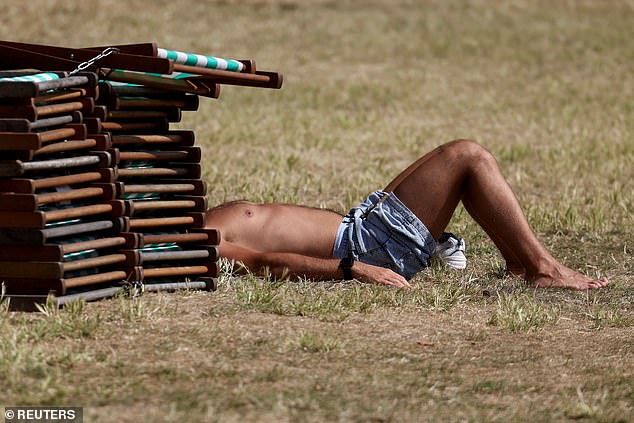 ENGLAND: A sunbather keeps his head in the shade with the help of a stack of deck chairs in Green Park, London on Monday