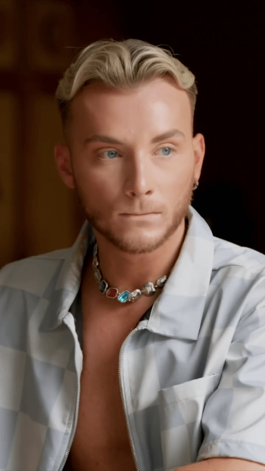 Harry Derbidge wearing a light gray checkered shirt and a colorful necklace.