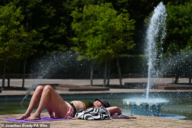 A woman sunbathes near the fountains at Battersea Park in South West London yesterday