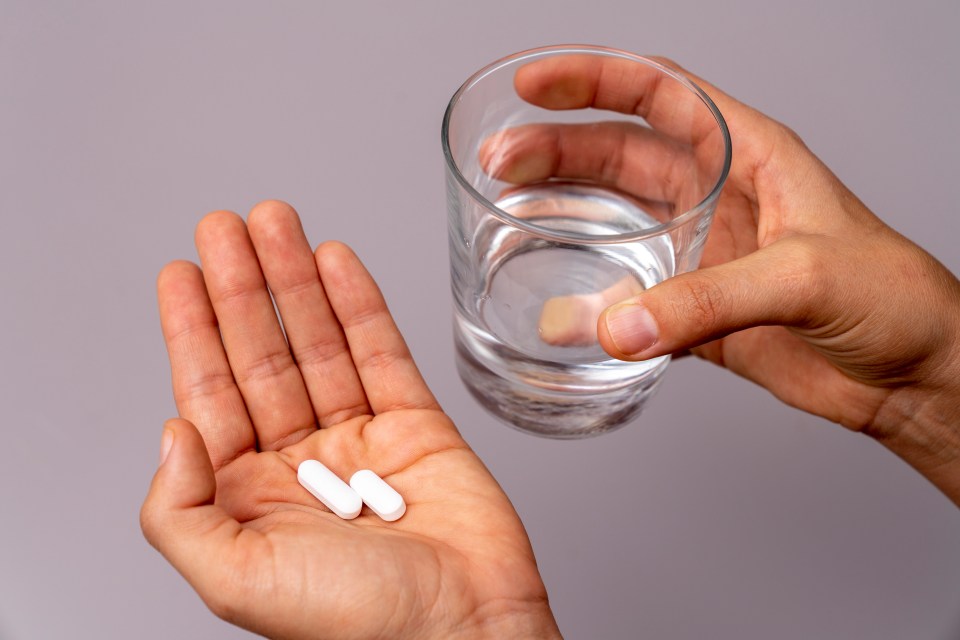 Hand holding two pills and a glass of water.