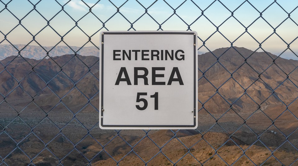 "Entering Area 51" sign behind a chain-link fence.