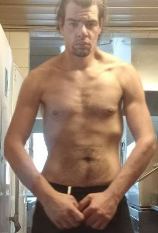 A shirtless man stands in front of a mirror.